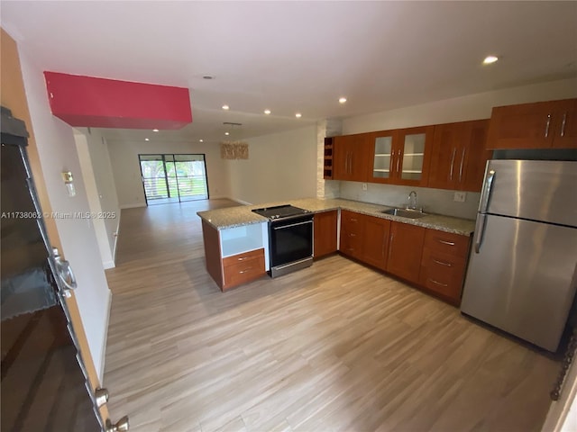 kitchen featuring sink, light stone counters, stainless steel refrigerator, kitchen peninsula, and range with electric cooktop