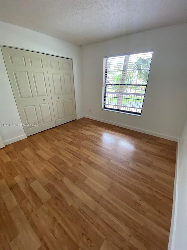 unfurnished bedroom featuring a textured ceiling, light hardwood / wood-style floors, and a closet