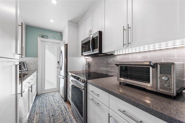 kitchen featuring stainless steel appliances, white cabinetry, tasteful backsplash, and dark stone counters