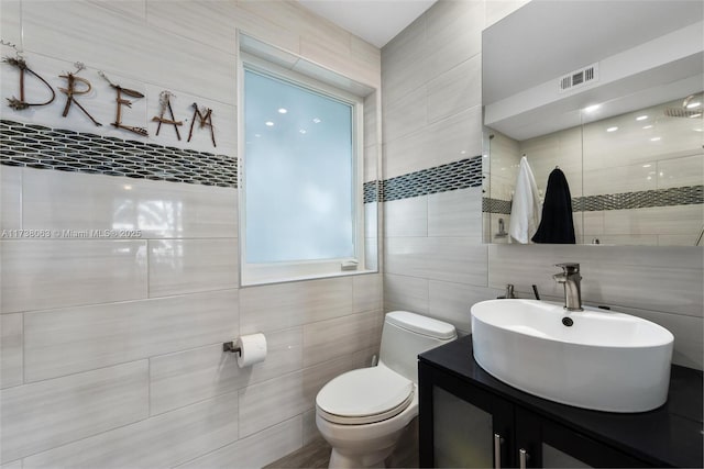 bathroom featuring vanity, tile walls, and toilet