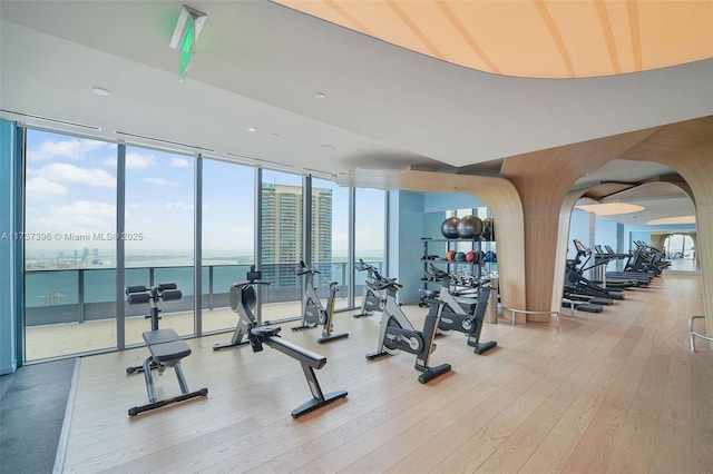 exercise room featuring a water view, a wall of windows, and hardwood / wood-style floors