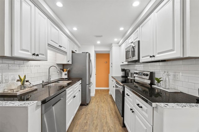 kitchen with appliances with stainless steel finishes, sink, white cabinets, backsplash, and light hardwood / wood-style flooring