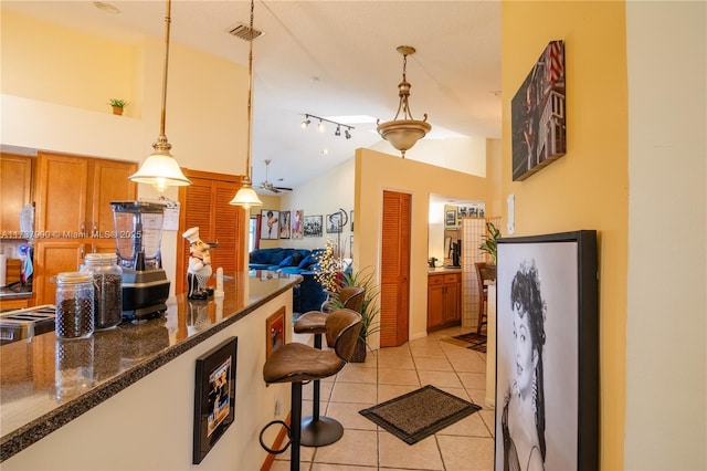 kitchen featuring pendant lighting, rail lighting, a breakfast bar, light tile patterned flooring, and dark stone counters