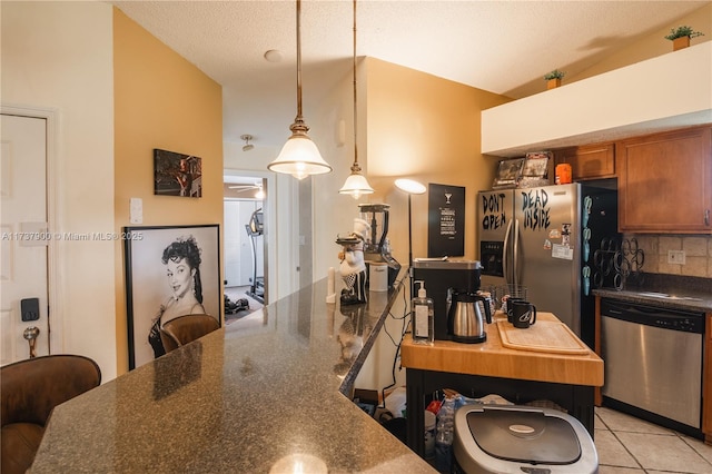 kitchen featuring appliances with stainless steel finishes, pendant lighting, tasteful backsplash, light tile patterned floors, and a textured ceiling