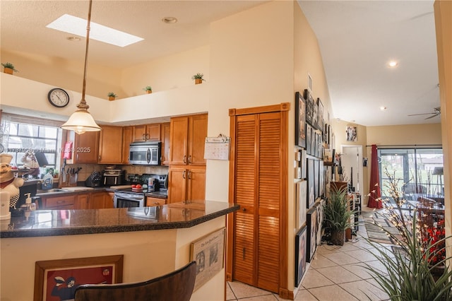 kitchen featuring appliances with stainless steel finishes, hanging light fixtures, plenty of natural light, vaulted ceiling with skylight, and kitchen peninsula