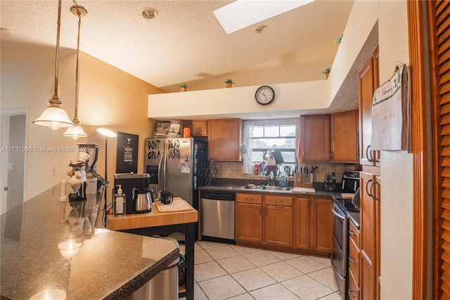 kitchen featuring light tile patterned flooring, sink, hanging light fixtures, appliances with stainless steel finishes, and vaulted ceiling with skylight