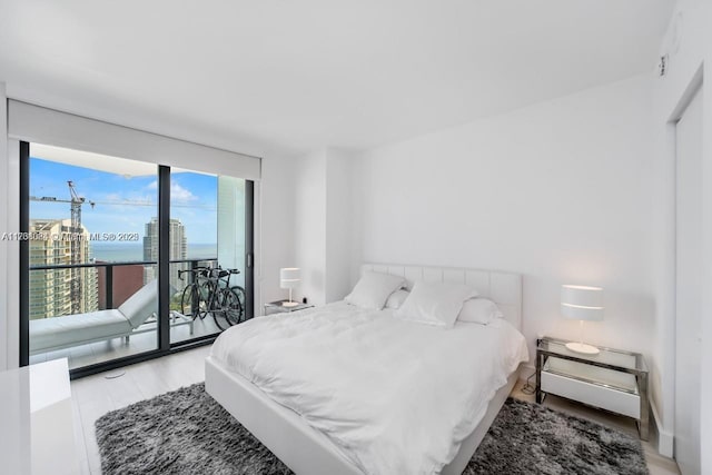 bedroom with a water view, expansive windows, access to exterior, and light wood-type flooring