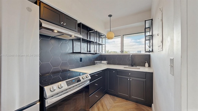 kitchen with appliances with stainless steel finishes, hanging light fixtures, light countertops, under cabinet range hood, and a sink