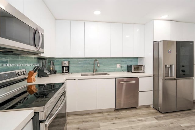 kitchen featuring sink, light hardwood / wood-style flooring, appliances with stainless steel finishes, white cabinets, and decorative backsplash