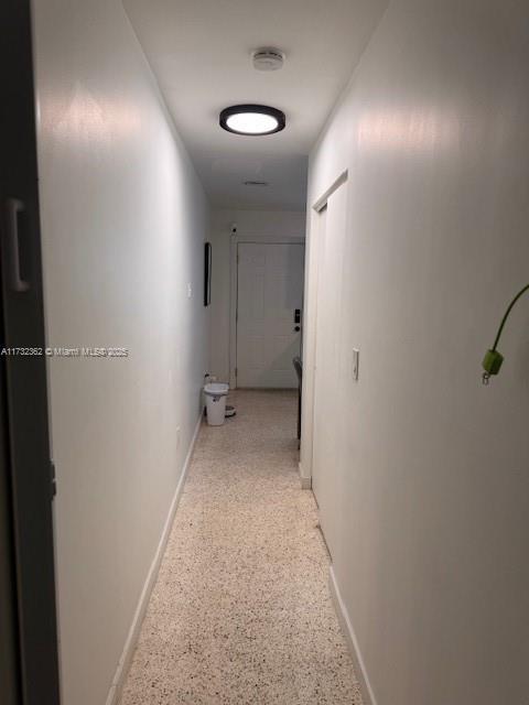 corridor featuring baseboards and light speckled floor