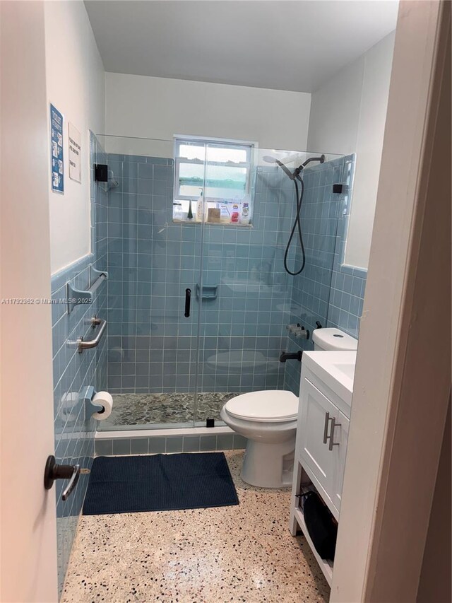 full bath with a shower stall, toilet, speckled floor, tile walls, and vanity
