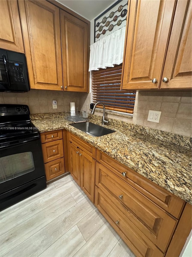 kitchen with sink, light hardwood / wood-style flooring, light stone counters, black appliances, and decorative backsplash