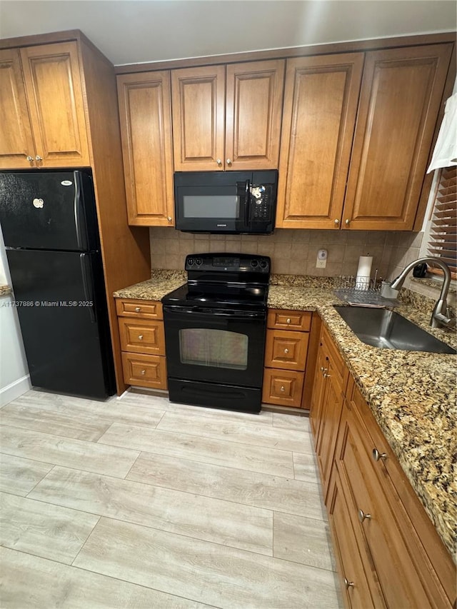 kitchen with sink, tasteful backsplash, light stone counters, black appliances, and light hardwood / wood-style floors