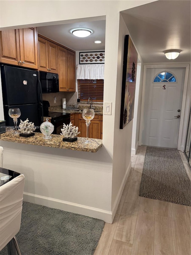 kitchen with sink, light hardwood / wood-style flooring, kitchen peninsula, light stone countertops, and black appliances