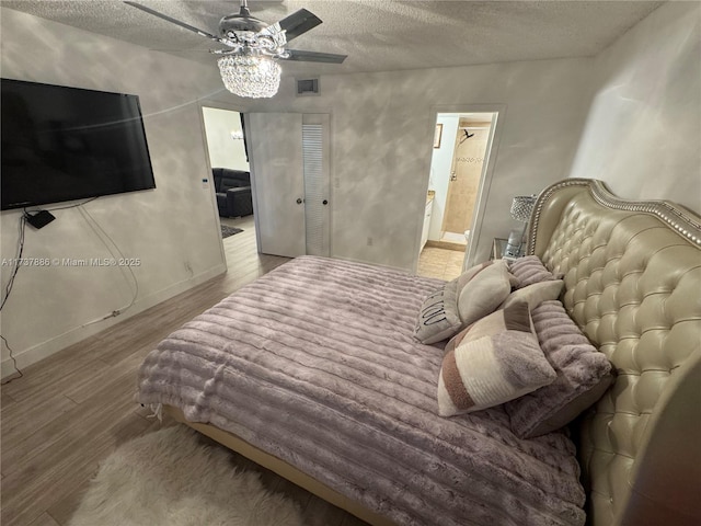 bedroom with ceiling fan, ensuite bathroom, light hardwood / wood-style floors, and a textured ceiling