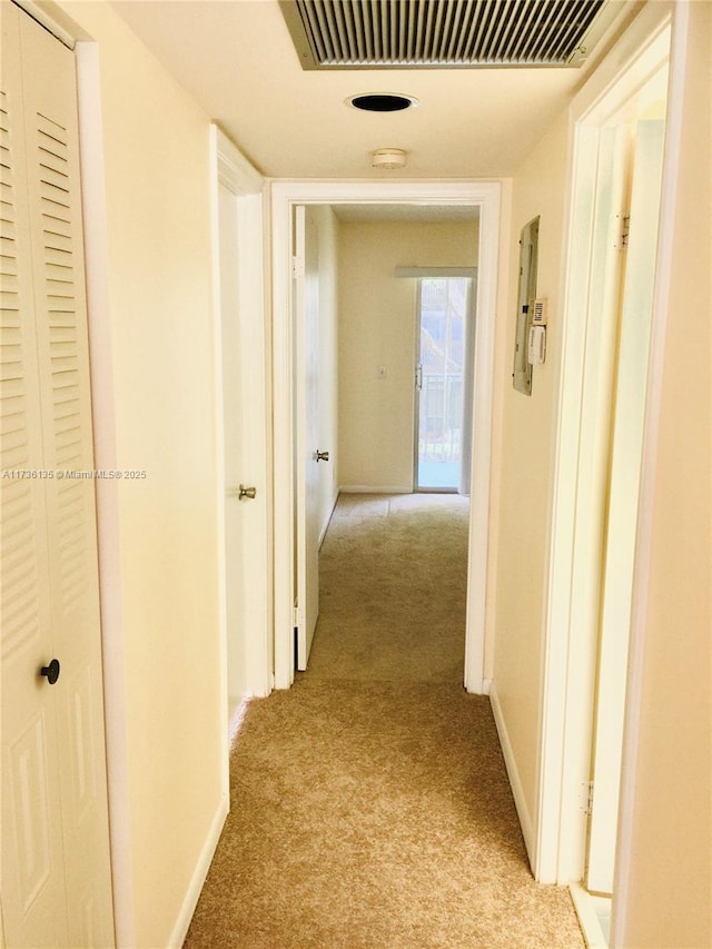 hallway with baseboards, visible vents, and light colored carpet