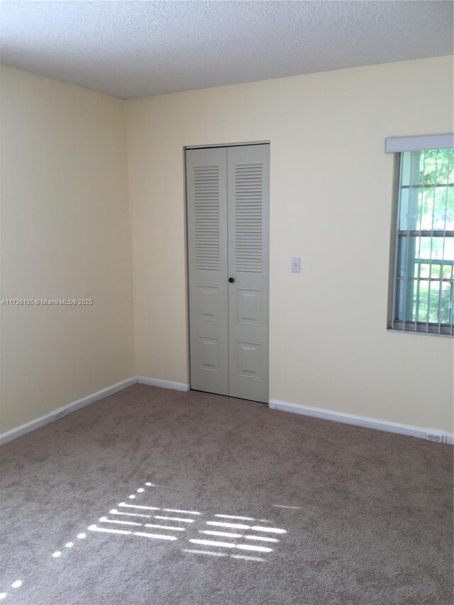 empty room with carpet floors, a textured ceiling, and baseboards