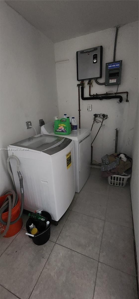 washroom featuring water heater, washer and dryer, and light tile patterned flooring