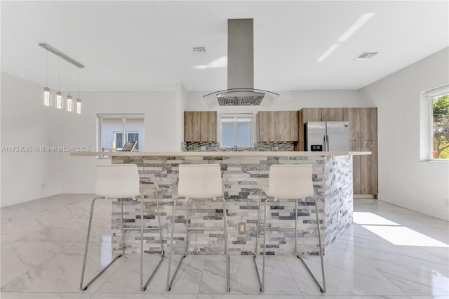 kitchen with pendant lighting, stainless steel fridge, range hood, and a breakfast bar area