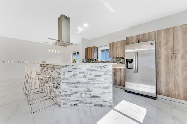 kitchen featuring stainless steel refrigerator with ice dispenser, island range hood, and tile walls