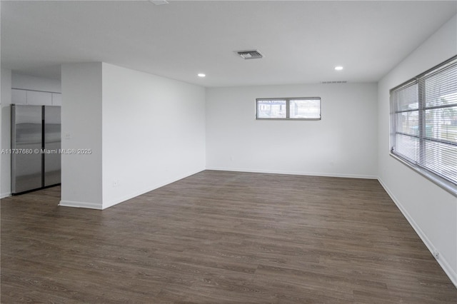 empty room with dark wood-type flooring, a healthy amount of sunlight, visible vents, and baseboards