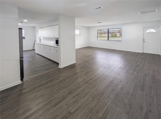 unfurnished living room featuring dark wood-style floors, visible vents, and baseboards