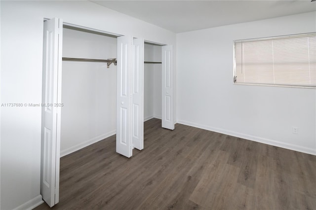 unfurnished bedroom featuring baseboards, wood finished floors, and multiple closets