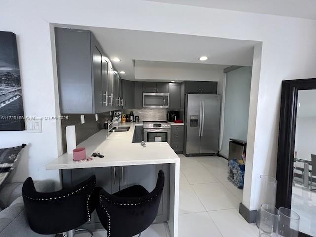 kitchen featuring a breakfast bar area, gray cabinets, kitchen peninsula, stainless steel appliances, and decorative backsplash