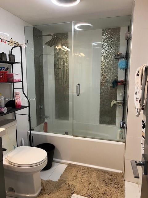 bathroom featuring combined bath / shower with glass door, tile patterned floors, and toilet