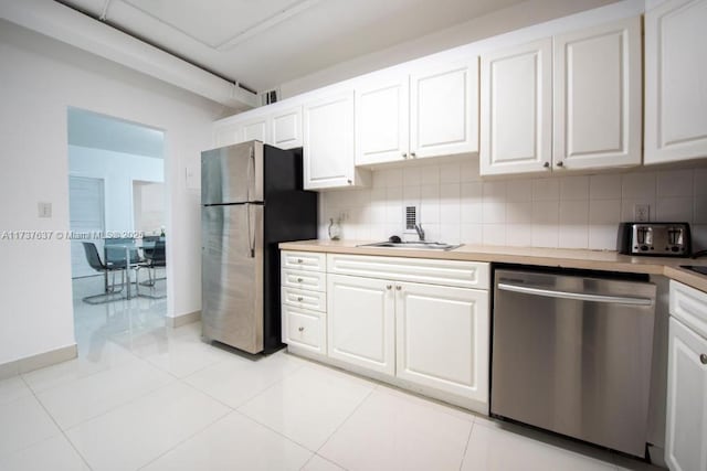 kitchen with light tile patterned floors, sink, white cabinetry, backsplash, and stainless steel appliances