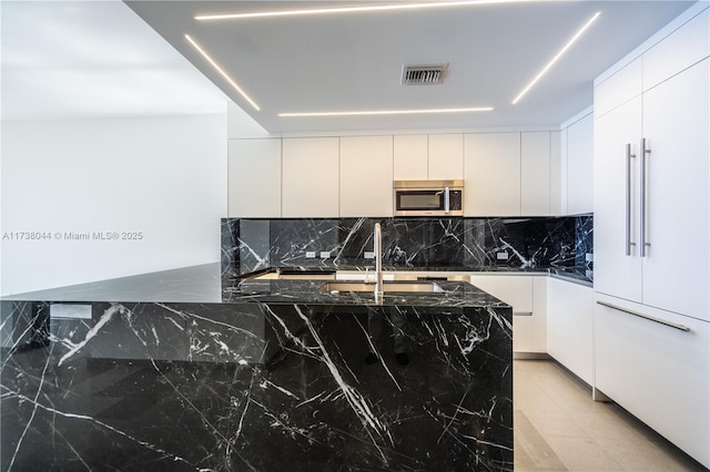 kitchen with sink, white cabinetry, paneled fridge, dark stone counters, and decorative backsplash