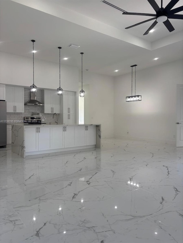 kitchen with hanging light fixtures, wall chimney range hood, white cabinets, and appliances with stainless steel finishes