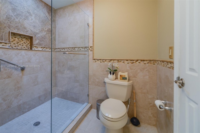 bathroom featuring toilet, tile patterned flooring, tile walls, and a tile shower