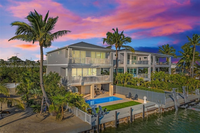 back house at dusk featuring a fenced in pool, a patio, a balcony, and a water view