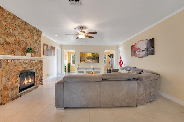 living room featuring light tile patterned floors, a stone fireplace, ornamental molding, and ceiling fan