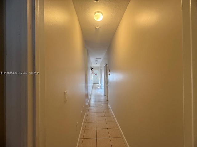 hallway featuring light tile patterned floors, baseboards, and a textured ceiling