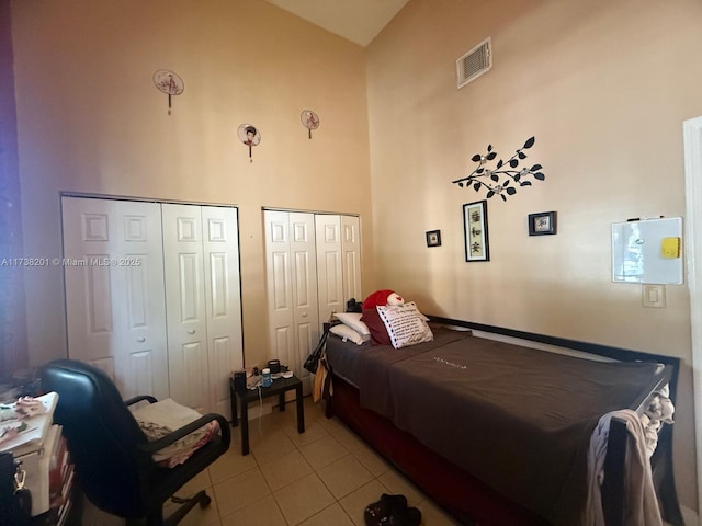 bedroom featuring multiple closets, visible vents, a high ceiling, and light tile patterned floors