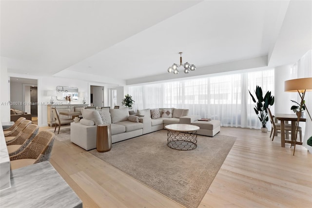 living room featuring an inviting chandelier, light hardwood / wood-style floors, and a raised ceiling