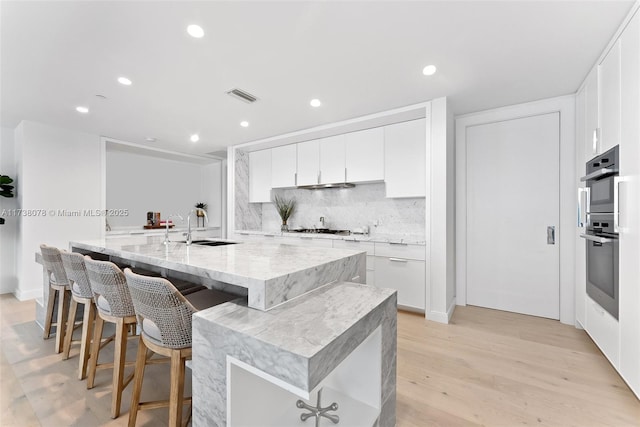 kitchen with white cabinetry, tasteful backsplash, a kitchen bar, and a center island with sink