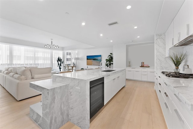 kitchen with a large island, sink, white cabinetry, light wood-type flooring, and beverage cooler