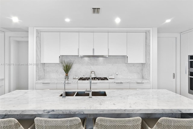 kitchen featuring sink, a breakfast bar area, white cabinets, and light stone counters