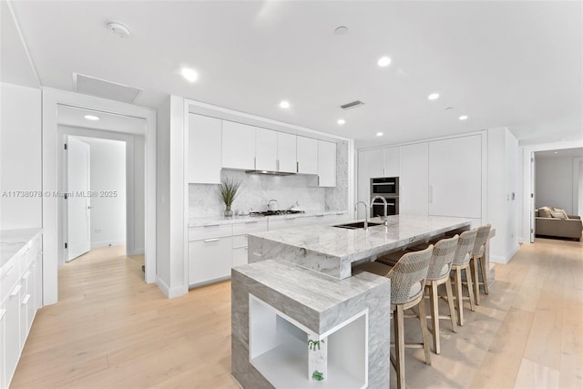 kitchen featuring tasteful backsplash, white cabinets, a kitchen bar, light hardwood / wood-style floors, and a center island with sink