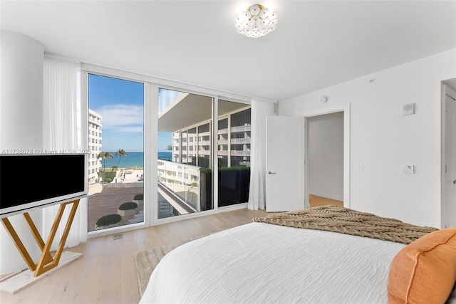 bedroom with a water view, light wood-type flooring, access to outside, and a wall of windows