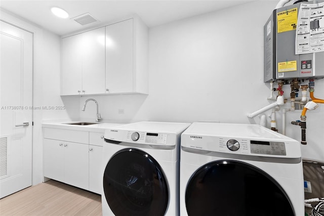 laundry room featuring sink, cabinets, light hardwood / wood-style flooring, washer and clothes dryer, and water heater