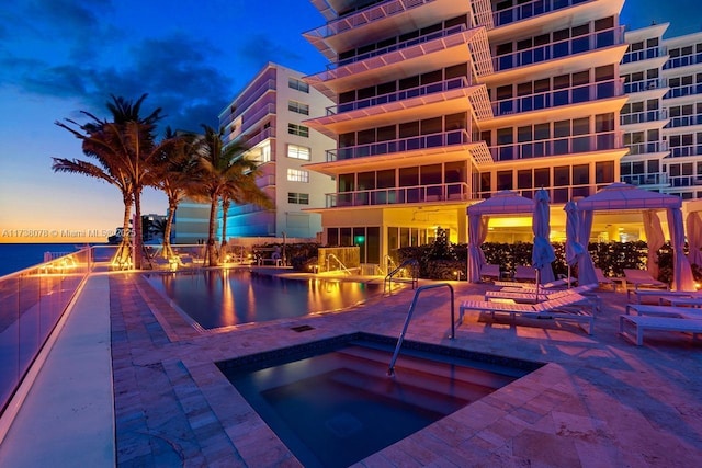 pool at dusk featuring a hot tub, a gazebo, and a patio area