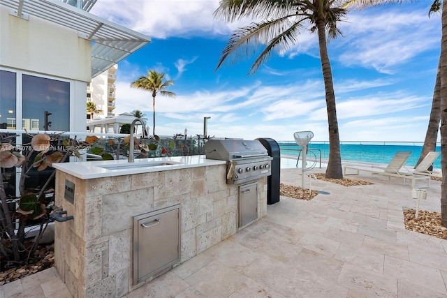 view of patio / terrace featuring area for grilling, a grill, sink, a water view, and a beach view