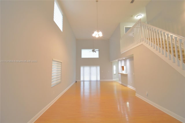 unfurnished living room with a high ceiling, ceiling fan with notable chandelier, and light hardwood / wood-style floors