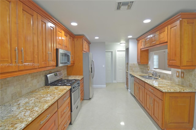 kitchen with tasteful backsplash, light stone countertops, appliances with stainless steel finishes, and sink