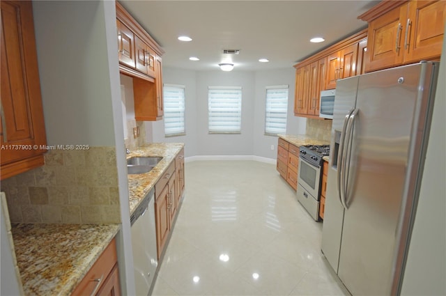 kitchen featuring a healthy amount of sunlight, appliances with stainless steel finishes, light stone countertops, and sink