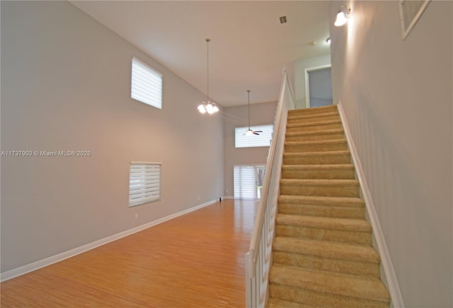 stairs with wood-type flooring, a chandelier, and a high ceiling